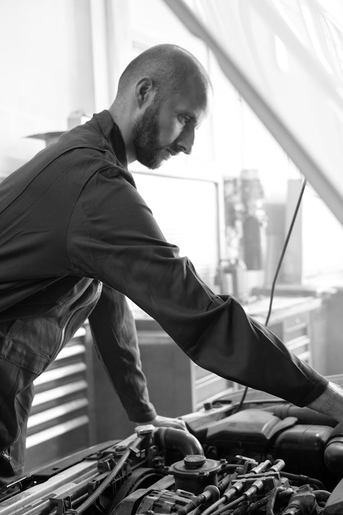 Monochrome photo of a mechanic checking a car engine in a workshop, highlighting attention to detail.